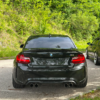 BMW M2 F87 Heckansicht in Schwarz auf einem Parkplatz mit sportlicher Tieferlegung und Doppelendrohr-Auspuffanlage.