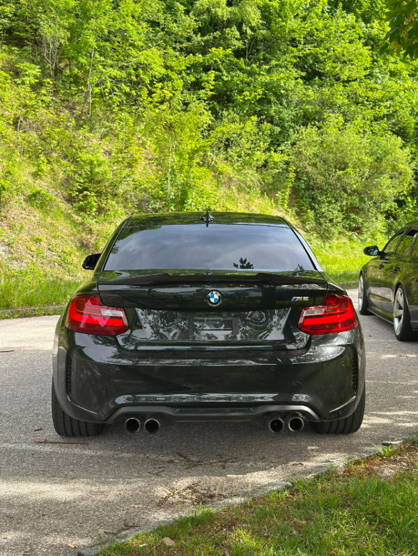 BMW M2 F87 Heckansicht in Schwarz auf einem Parkplatz mit sportlicher Tieferlegung und Doppelendrohr-Auspuffanlage.